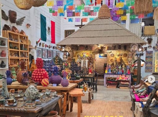 Interior de la galería con papel picado, palapa y mesas de artesanías