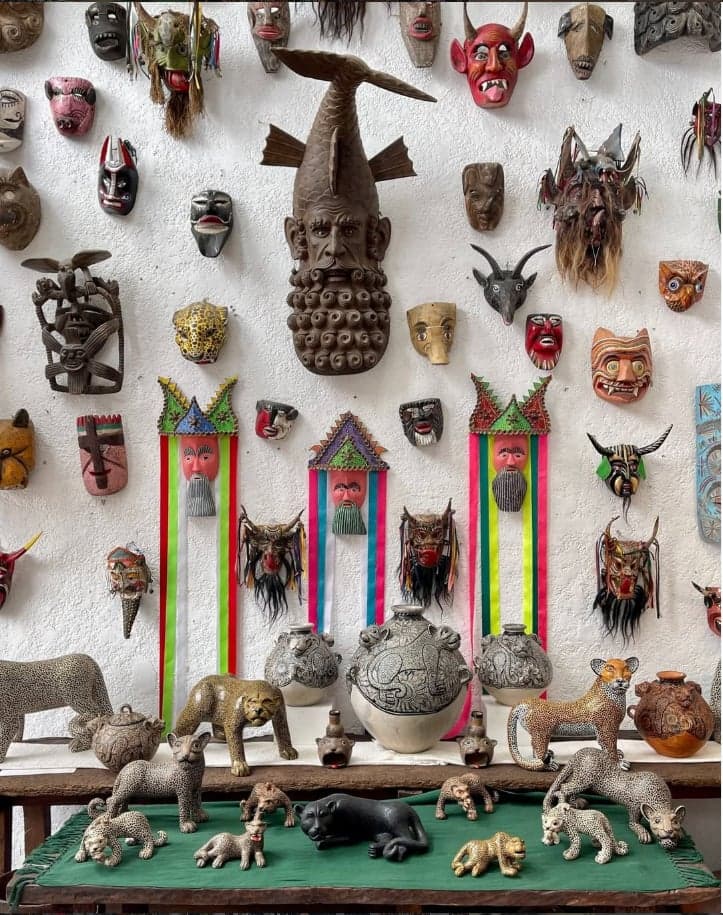 Muro de máscaras mexicanas artesanales junto a esculturas de jaguares y pumas